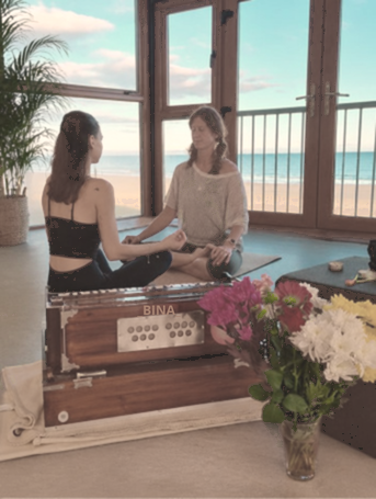 Jessica Hogan in a yoga session with a harmonium and flowers, sea view behind